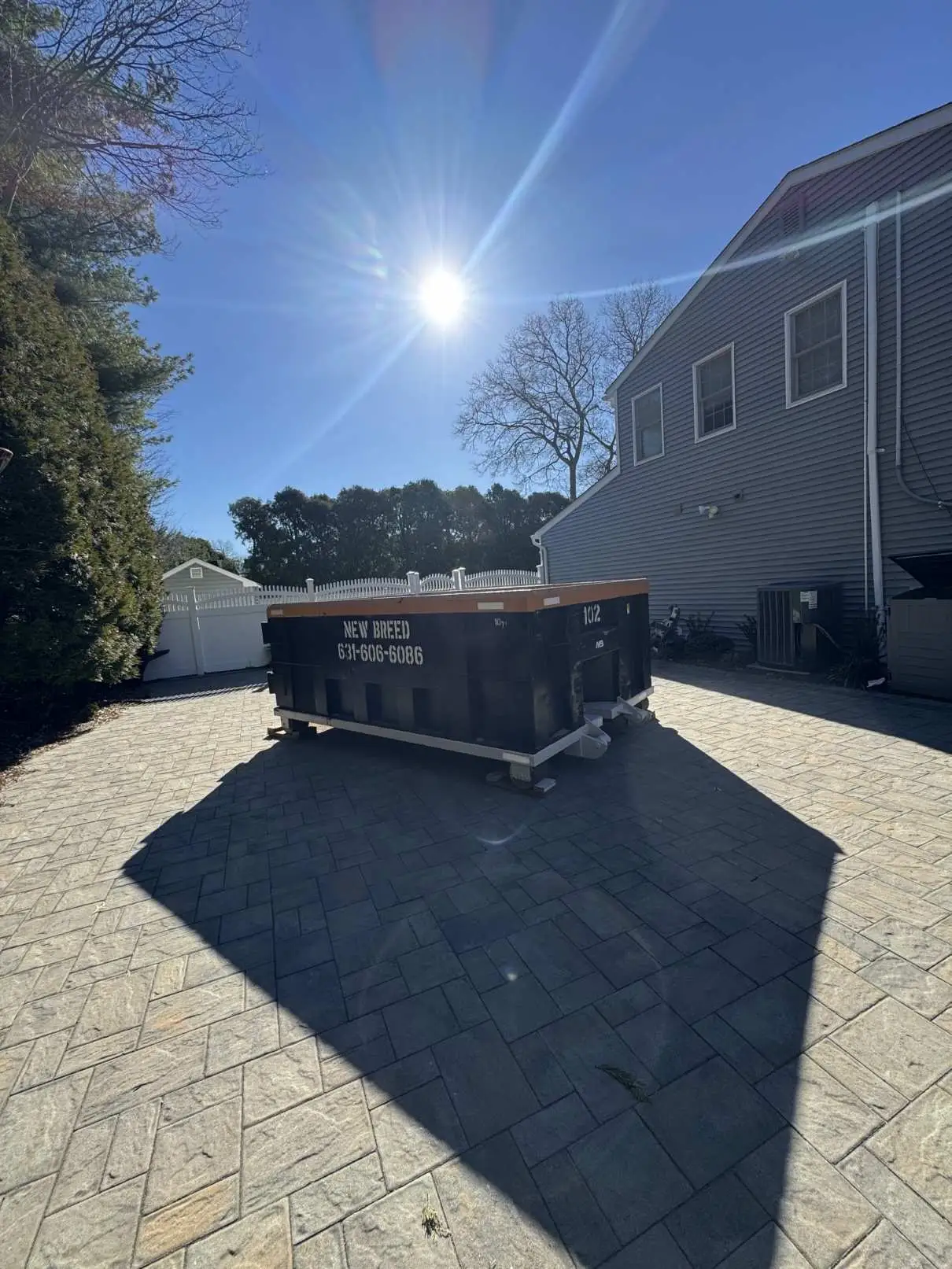 10-Yard Dumpster with Driveway Protection A 10-yard New Breed Haulage dumpster placed safely on wood planks to protect a paver driveway.